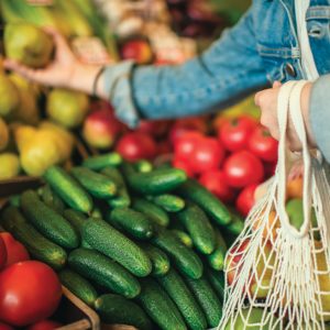 Close-up of woman holding an ecologically friendly reusable bag grabbing fruit and vegetables at a farmers market